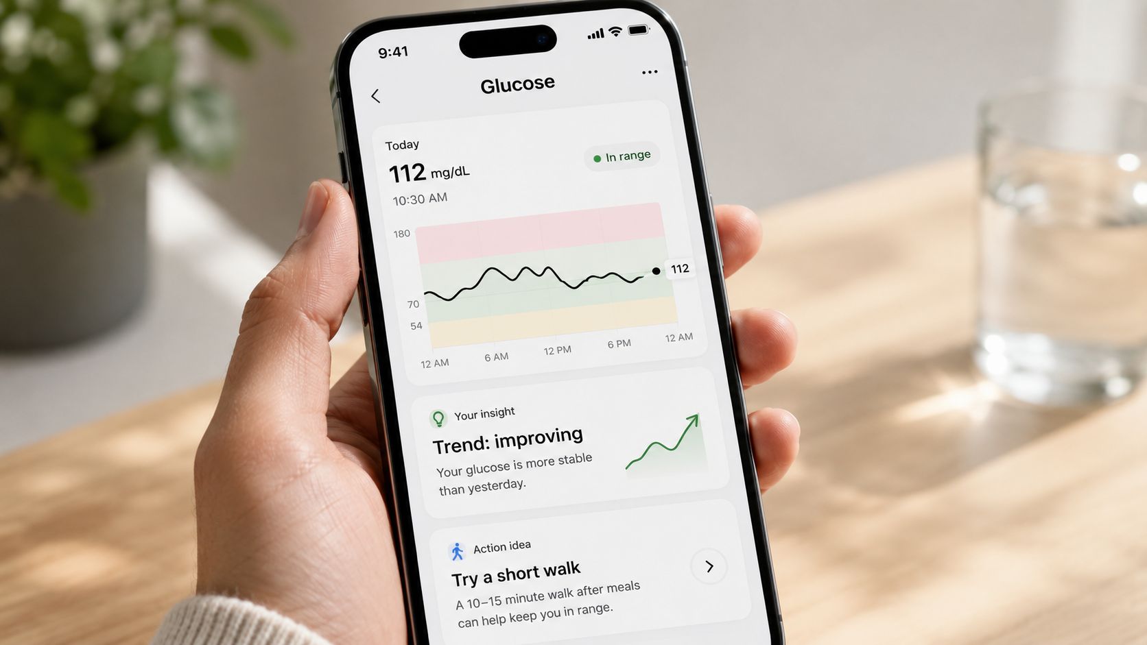 A person holding a smartphone displaying a glucose monitoring app interface showing health data and trends.